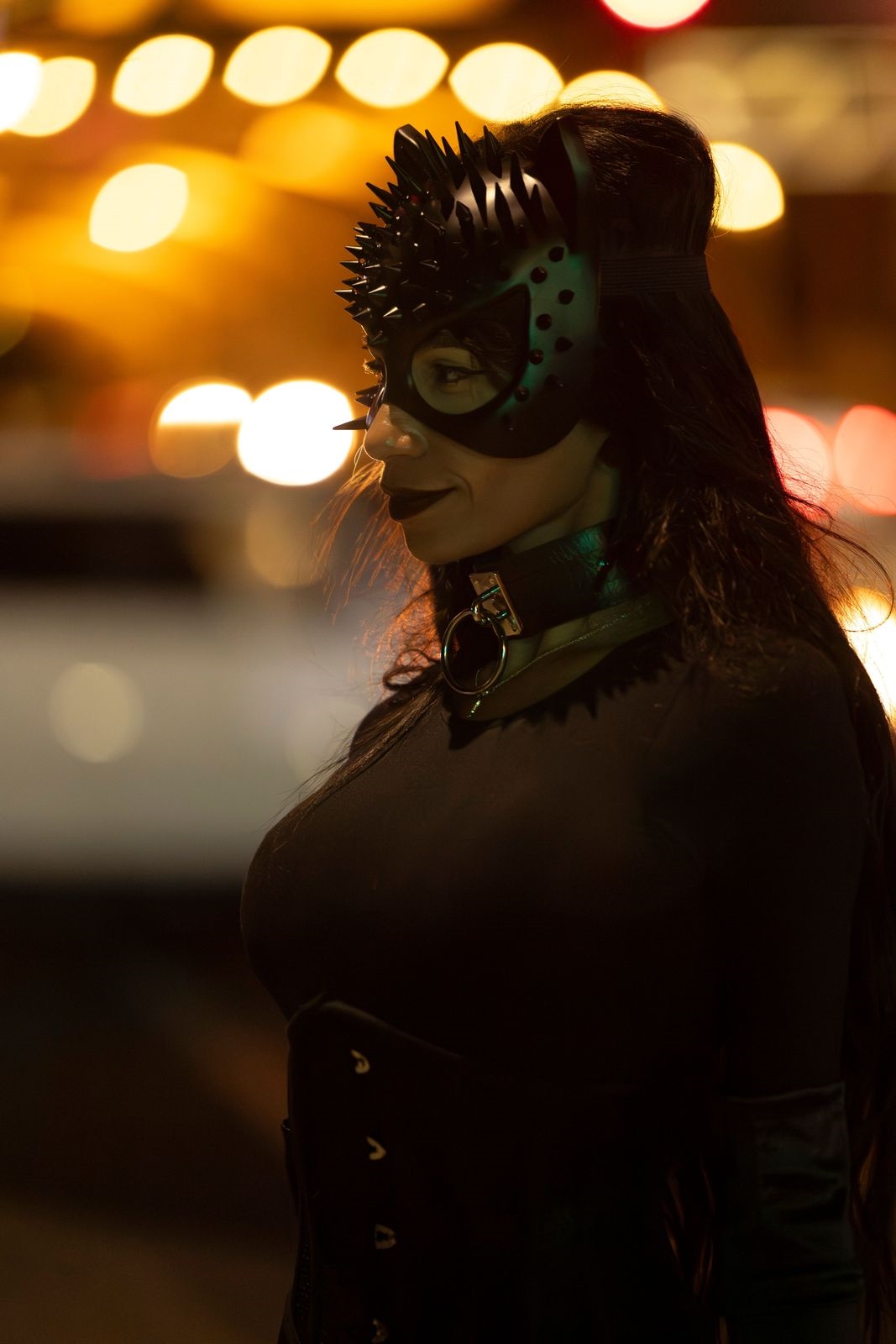 Woman in a black cat mask with city lights behind her at night, illustrative stock photo