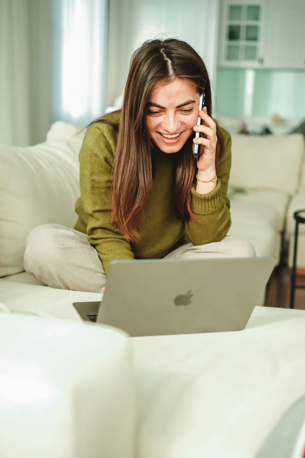 Smiling woman on a sofa with a laptop and phone, illustrative photo of a model