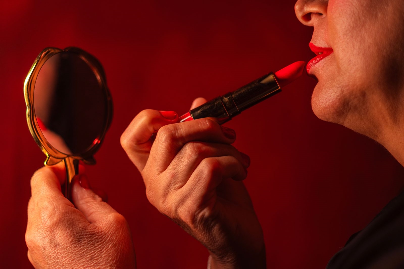 Glamorous mature woman applying bright red lipstick while holding a gold hand mirror