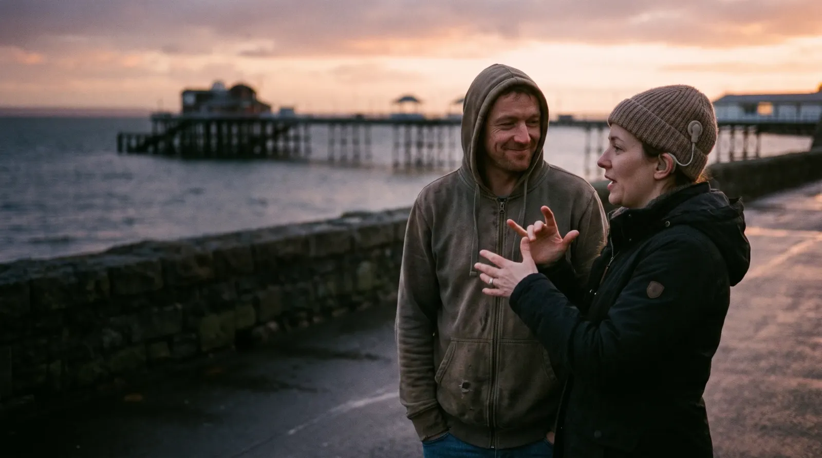 A couple on the Mumbles seafront at sunset; the woman has a cochlear implant and signs as she talks