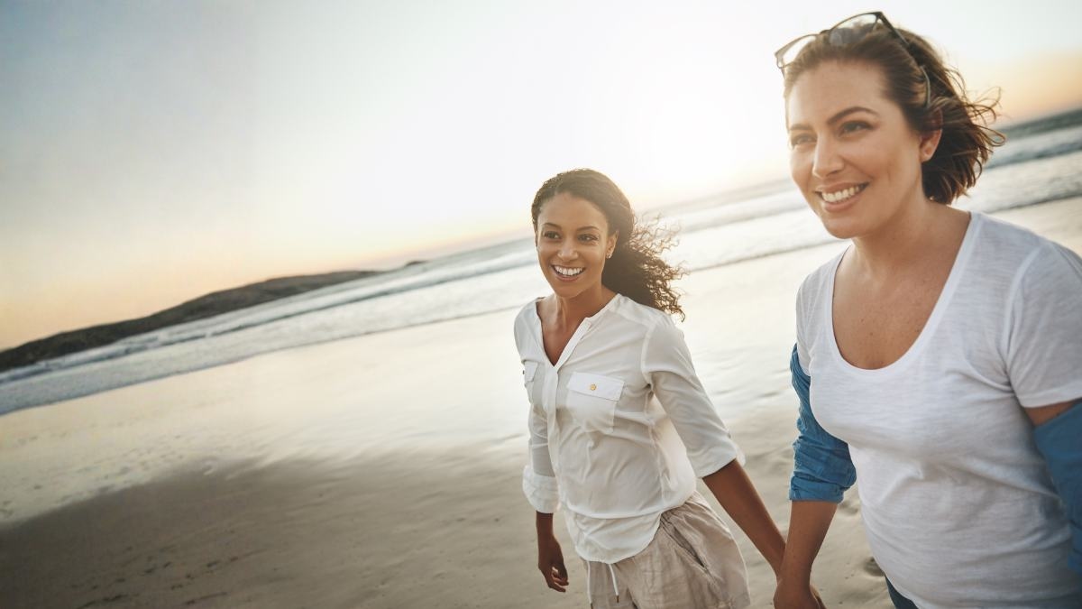 Two women walking together along a beach at sunset, holding hands
