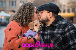 A joyful couple sharing their first kiss whilst on a dog walking first date in the city while their dog looks into the camera.