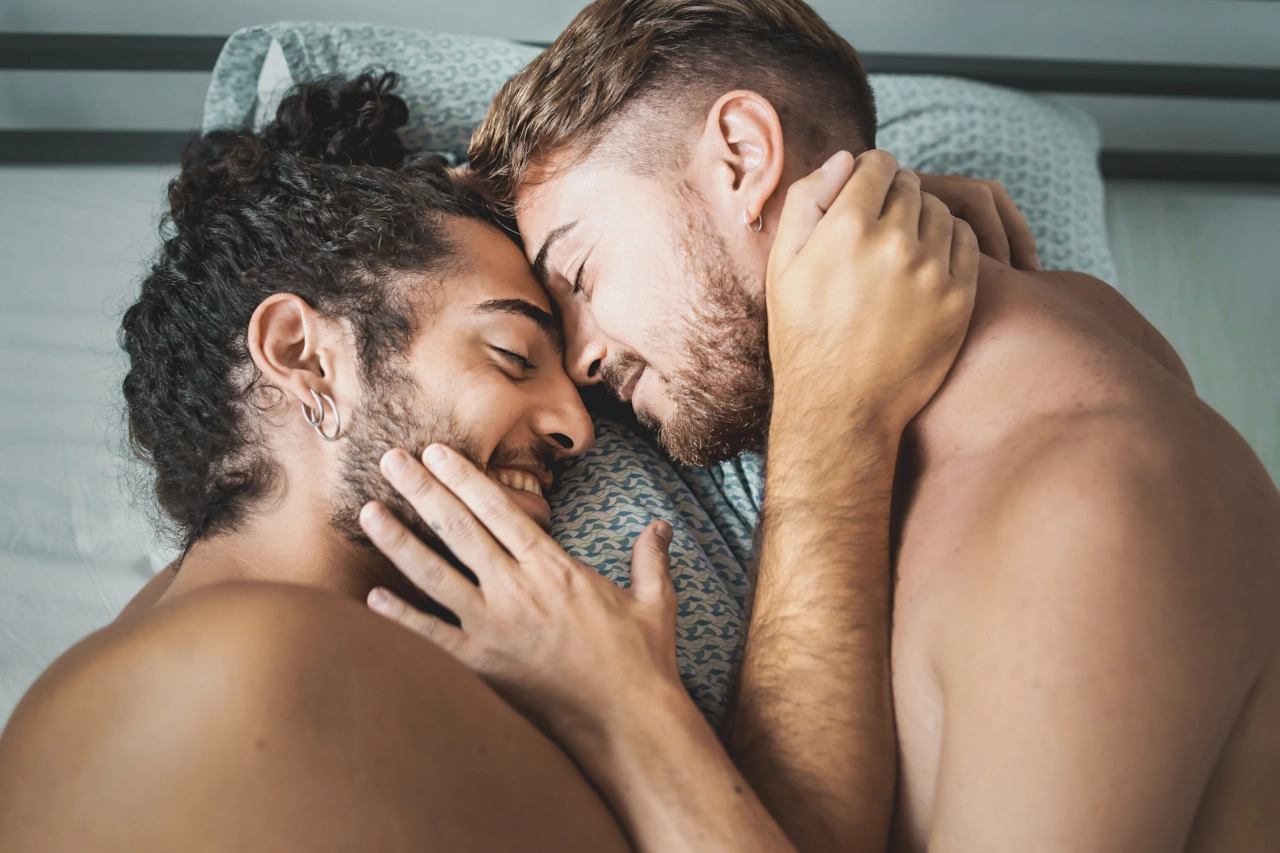 Dos hombres tumbados frente a frente en una cama, riéndose.