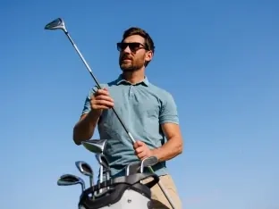 A male golfer in sunglasses choosing a club from his bag against a blue sky