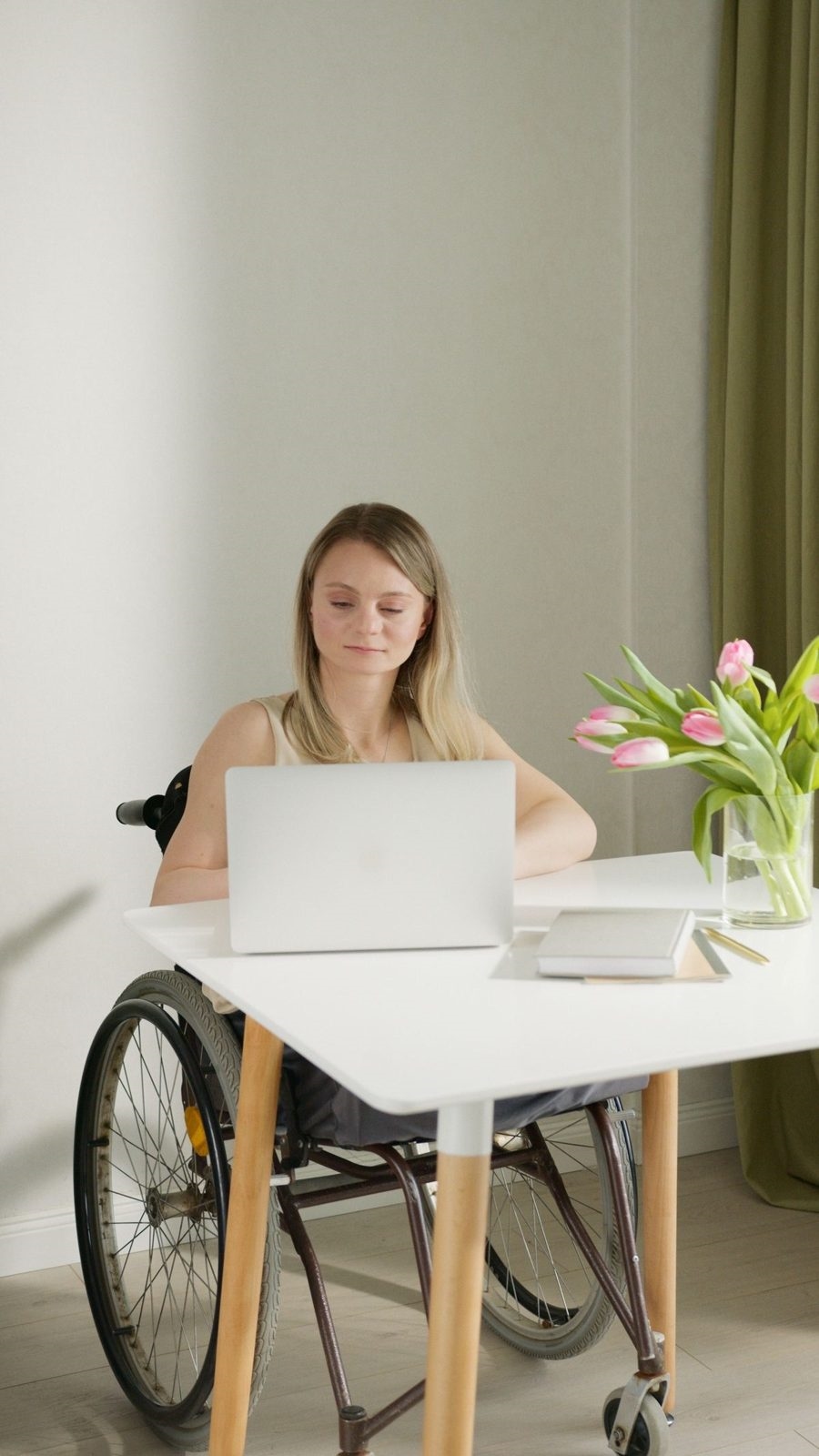 A woman in a wheelchair smiling at her laptop at home