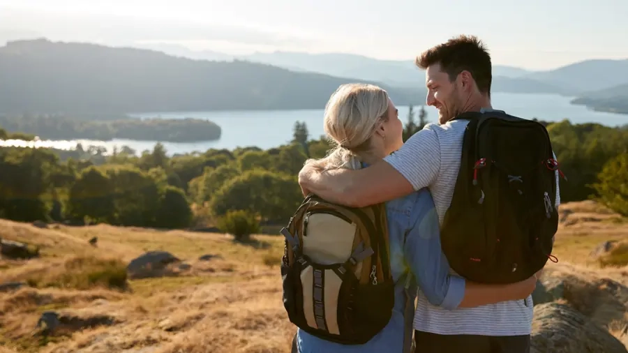 A couple with rucksacks pausing on a hillside above a lake