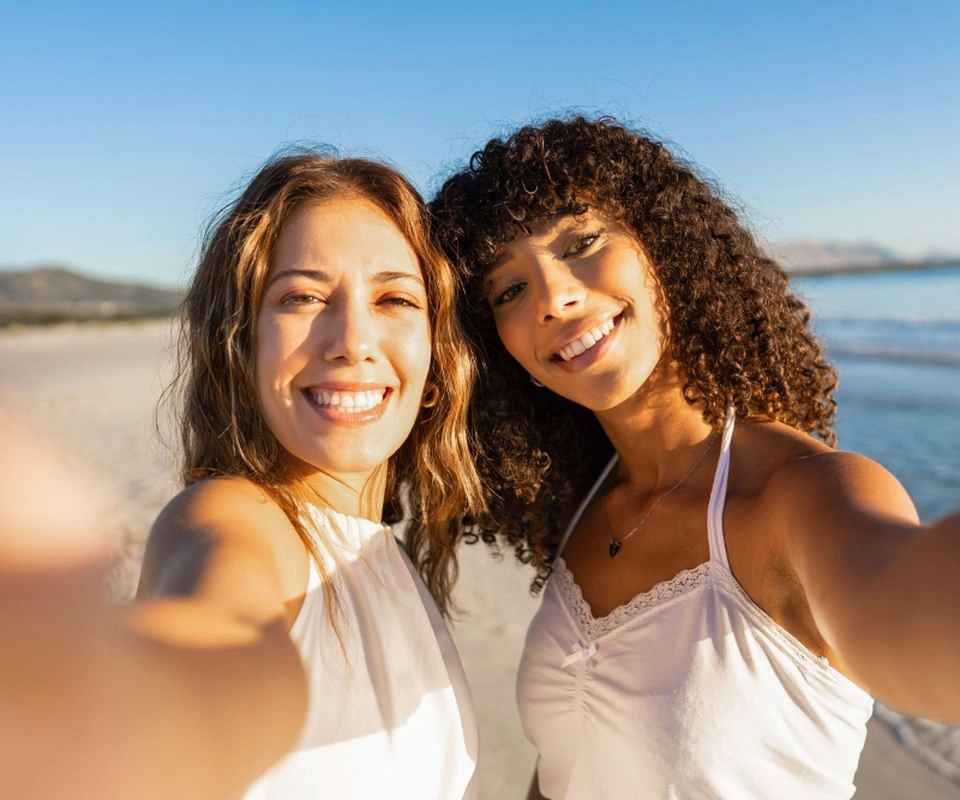 Two women smile for a selfie on a sunny beach