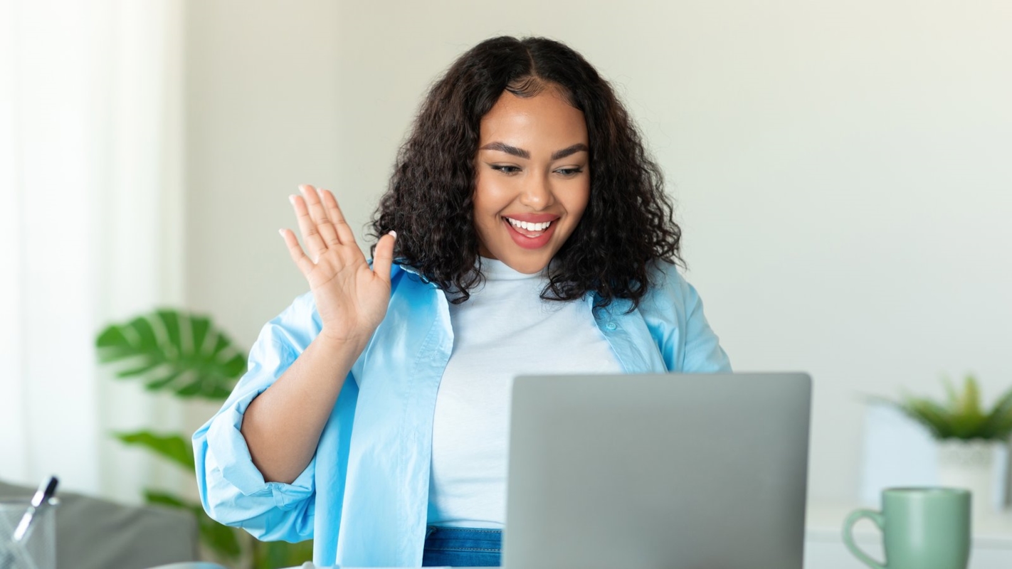 A woman smiling and waving at her laptop while working from home