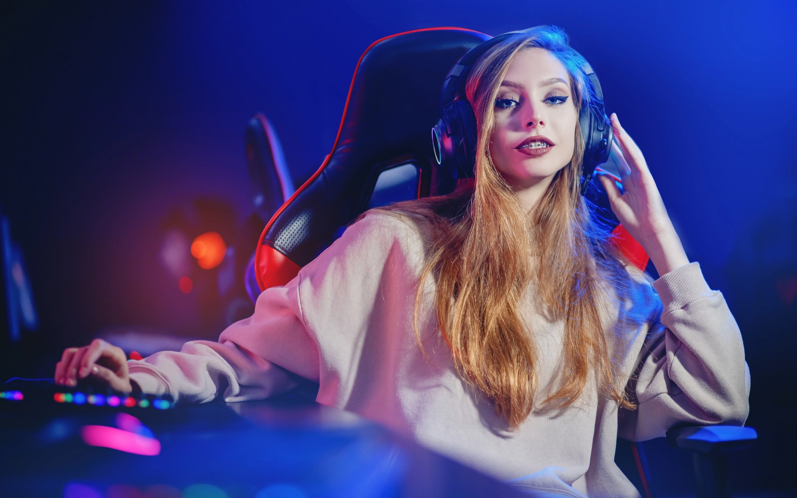 A woman with long hair and a headset at a gaming desk in blue light