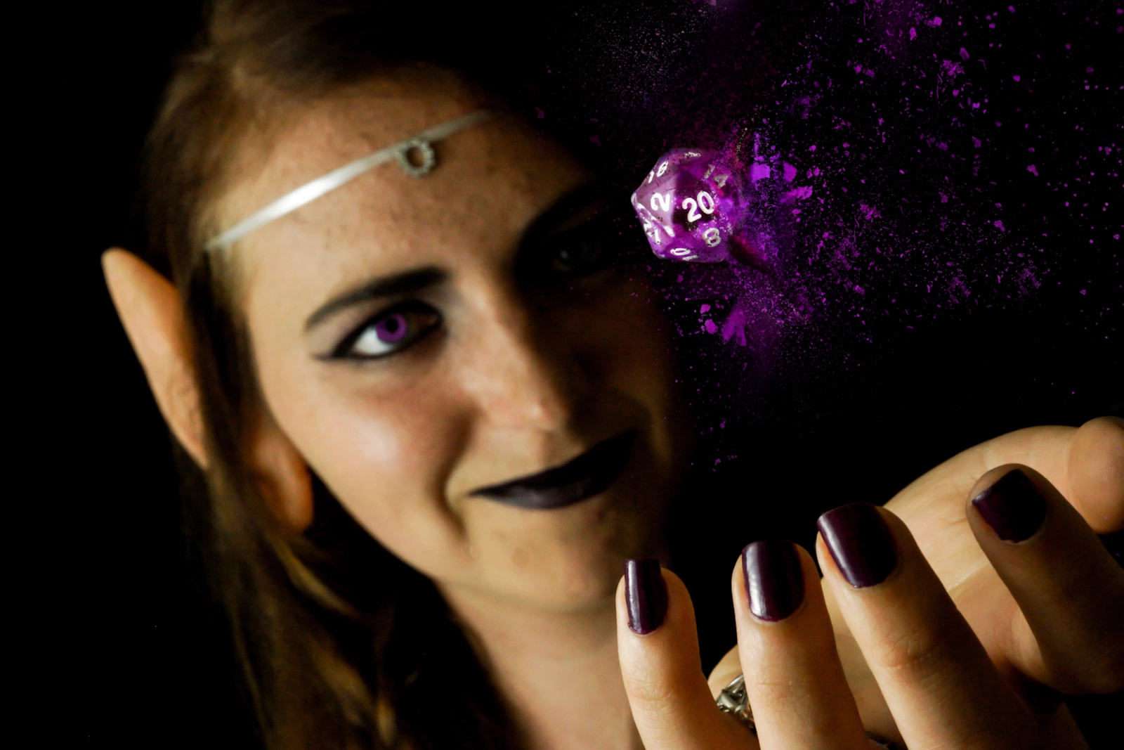 A woman with elf ears and a circlet holding a glowing d20 die