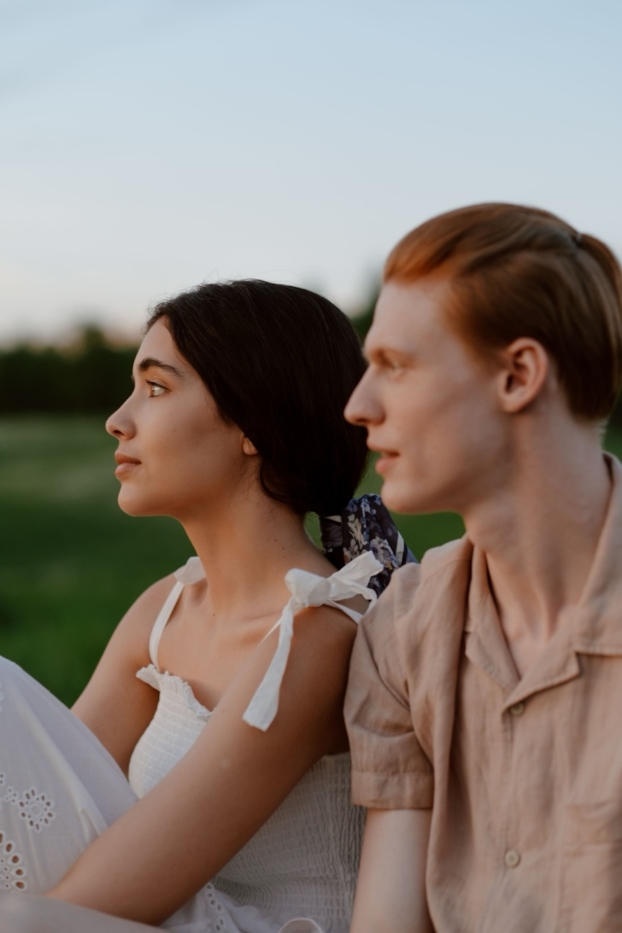 A couple sits together in a field at twilight