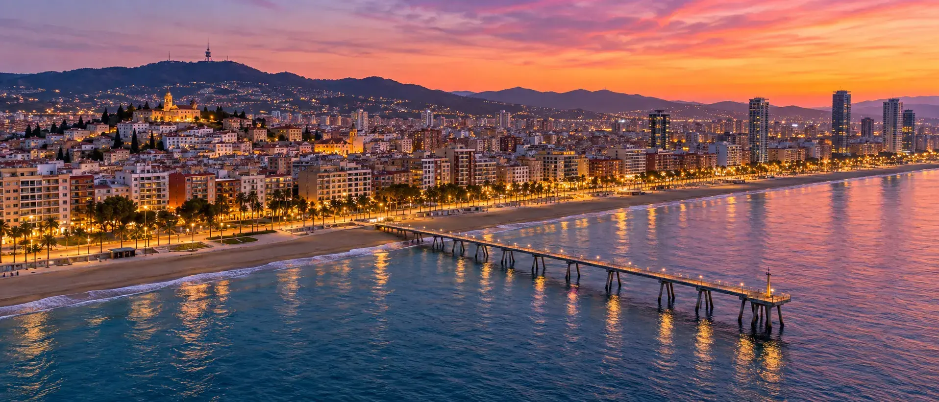 Badalona al atardecer con el Pont del Petroli adentrándose en el mar, la playa y el paseo marítimo iluminados