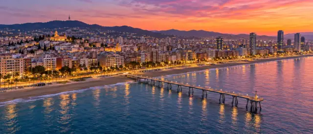 Badalona al atardecer con el Pont del Petroli adentrándose en el mar, la playa y el paseo marítimo iluminados