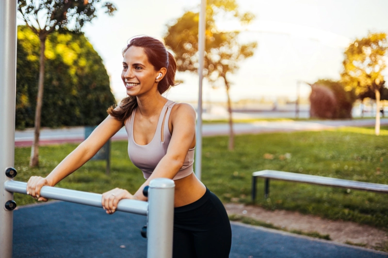 A smiling woman leaning on the bars at an outdoor gym in a park