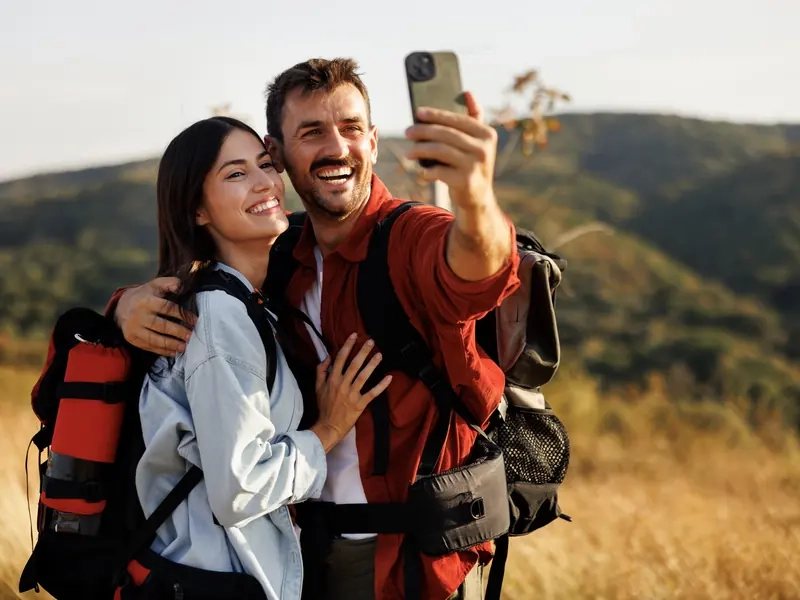 A laughing couple with hiking backpacks taking a selfie in golden hills