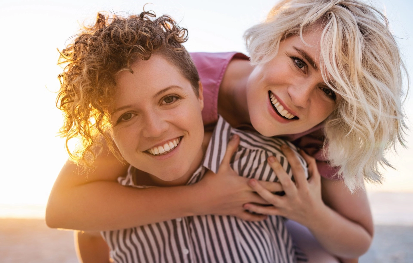 Two women laughing on a beach, one carrying the other on her back