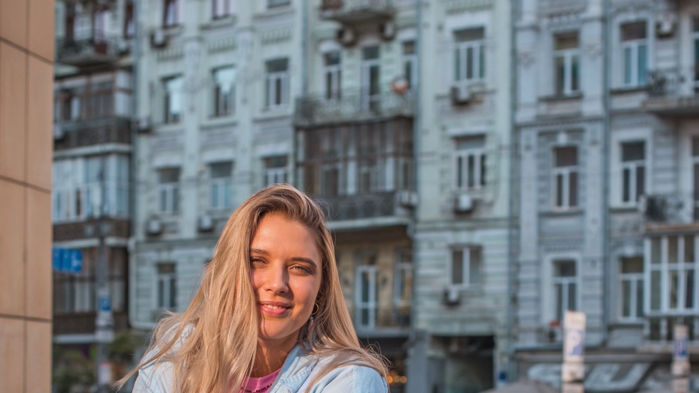 A woman smiling on a city street, holding a coffee