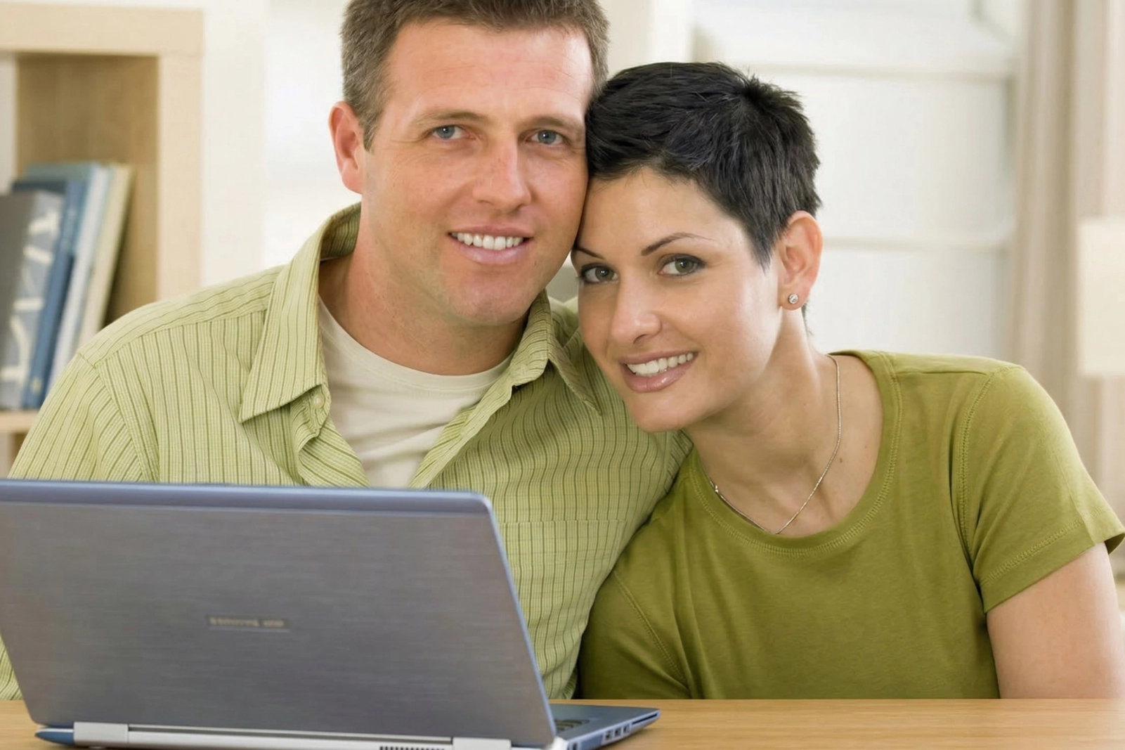 A smiling couple sitting close together in front of a laptop at home