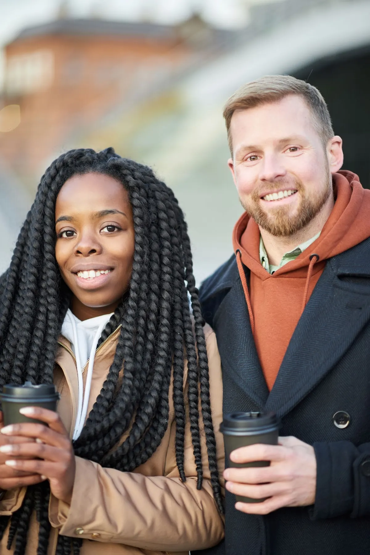 Smiling friends holding coffee cups outdoors, illustrative photo of models