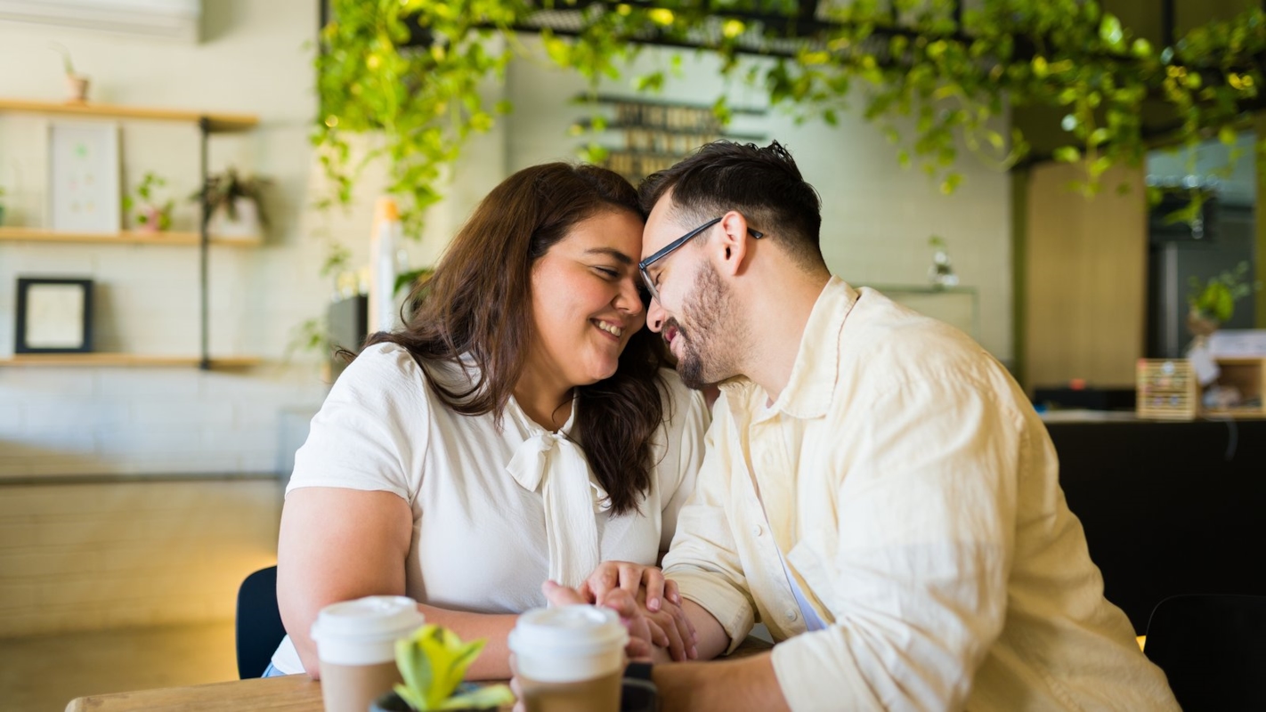 A couple sitting close together at a cafe table, foreheads touching
