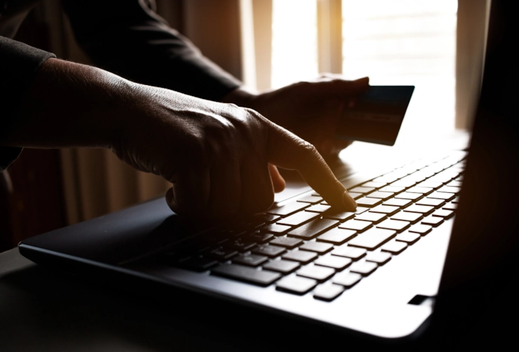 A person holding a bank card while typing on a laptop in a dim room