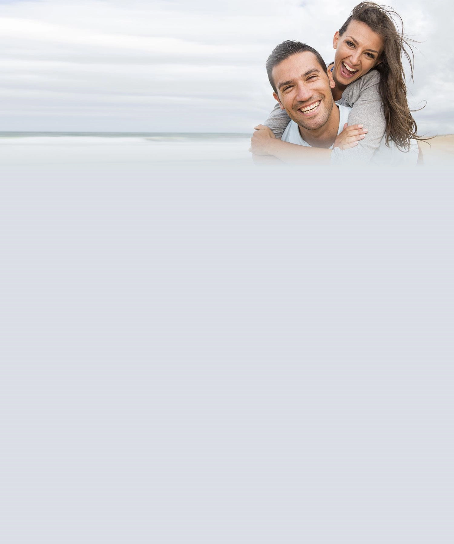 A smiling mum and dad sharing a piggyback on the beach