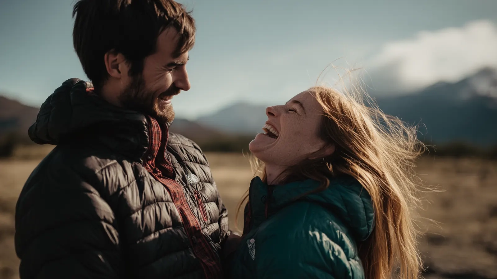 A couple laughing together on a windswept mountain hike