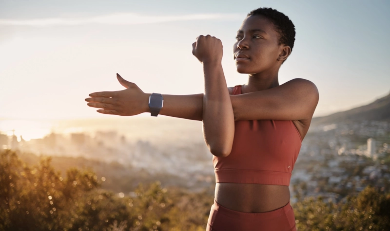 A woman stretching her arm on a hillside above a city at sunrise