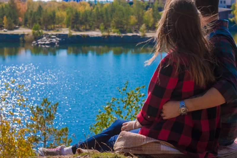 Couple sitting together on the shore of a bright blue mountain lake surrounded by forest