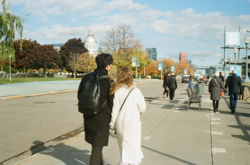 Couple walking side by side along a busy city waterfront path on a sunny day