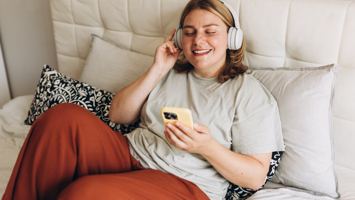 A woman relaxing at home with headphones, smiling at her phone