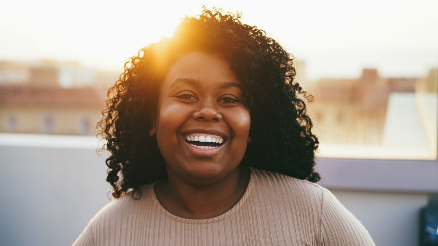 A woman laughing confidently on a rooftop at golden hour