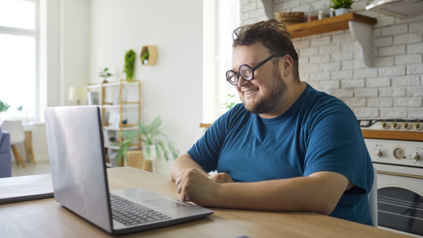 A man smiling while working on his laptop at a kitchen table