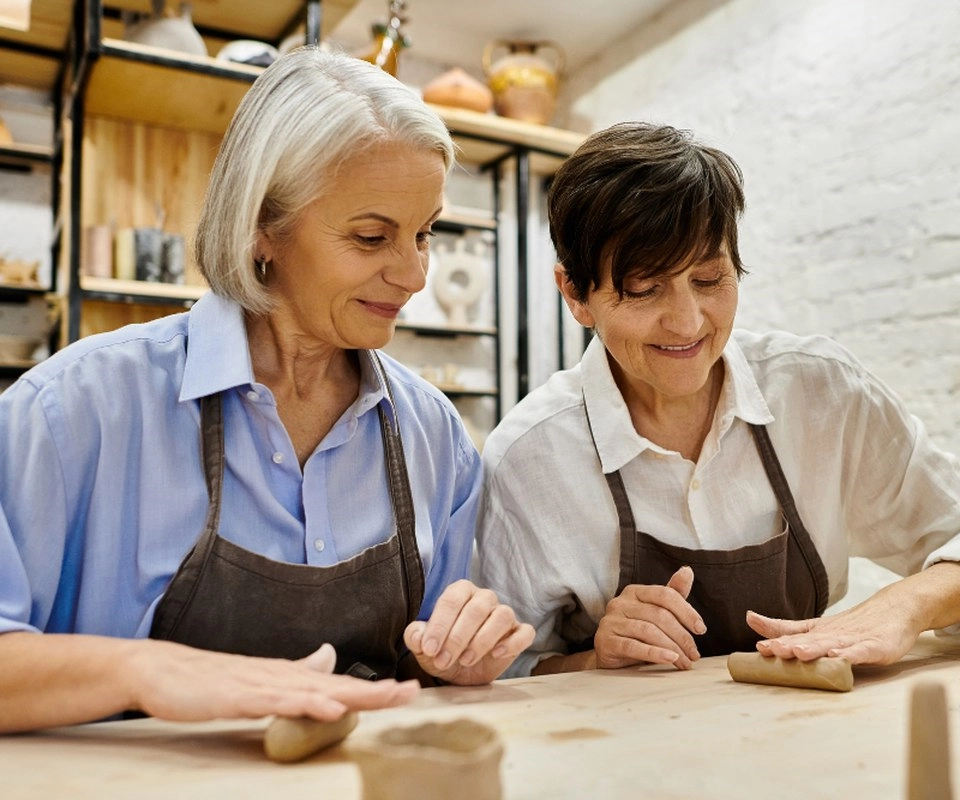 Two women in aprons work side by side at a craft table