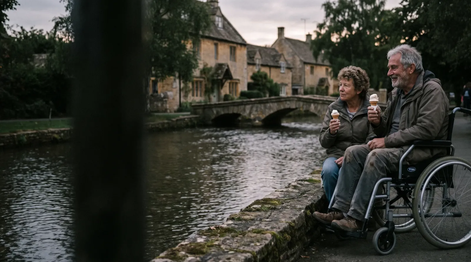 A couple with ice creams by the river at Bourton-on-the-Water; the man is a wheelchair user