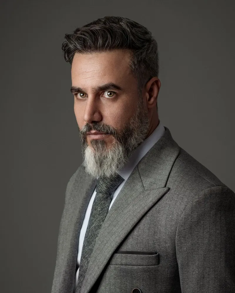 Bearded man in a tailored grey suit with a calm, assured look