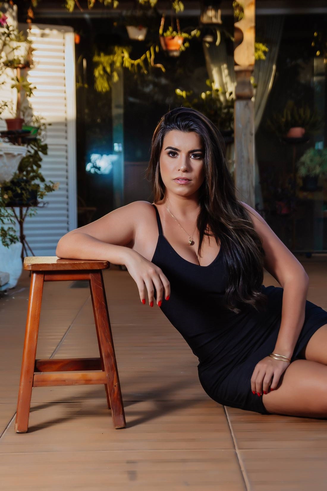 A woman in a black dress leaning on a bar stool on a tiled patio, illustrative photo of a model