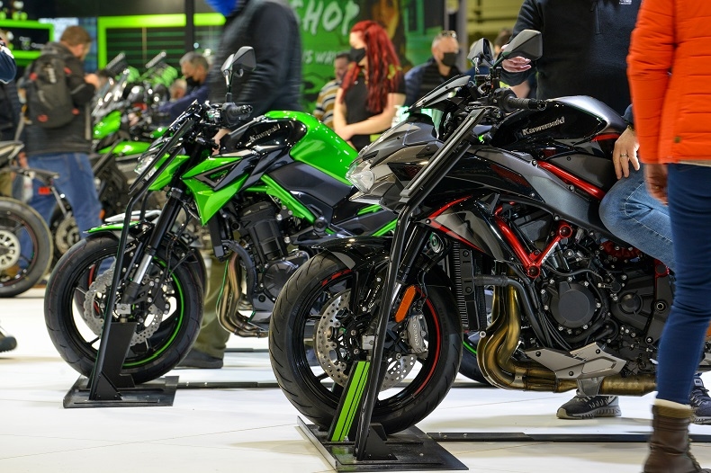 Motorcycles on display stands at a bike show, with visitors walking the floor