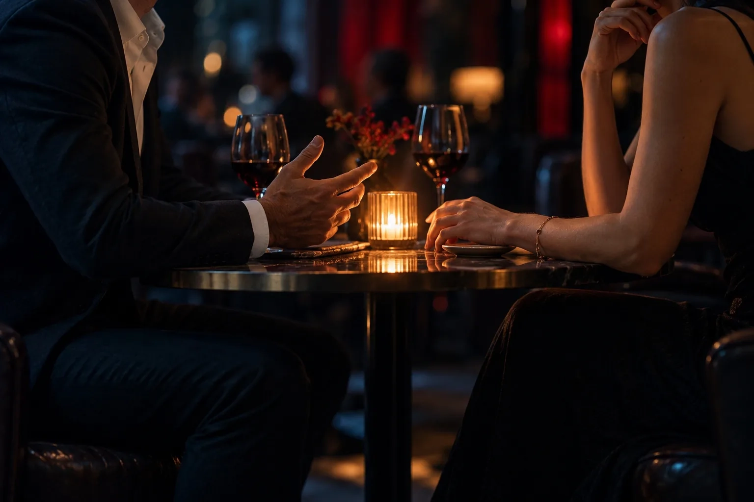 Dos personas conversan frente a frente en una mesa de restaurante en penumbra, con las manos cerca sobre la mesa
