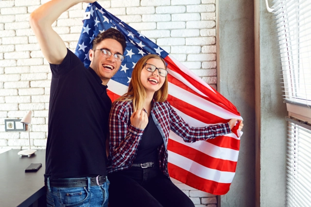 A laughing couple holding the American flag up in a sunny loft