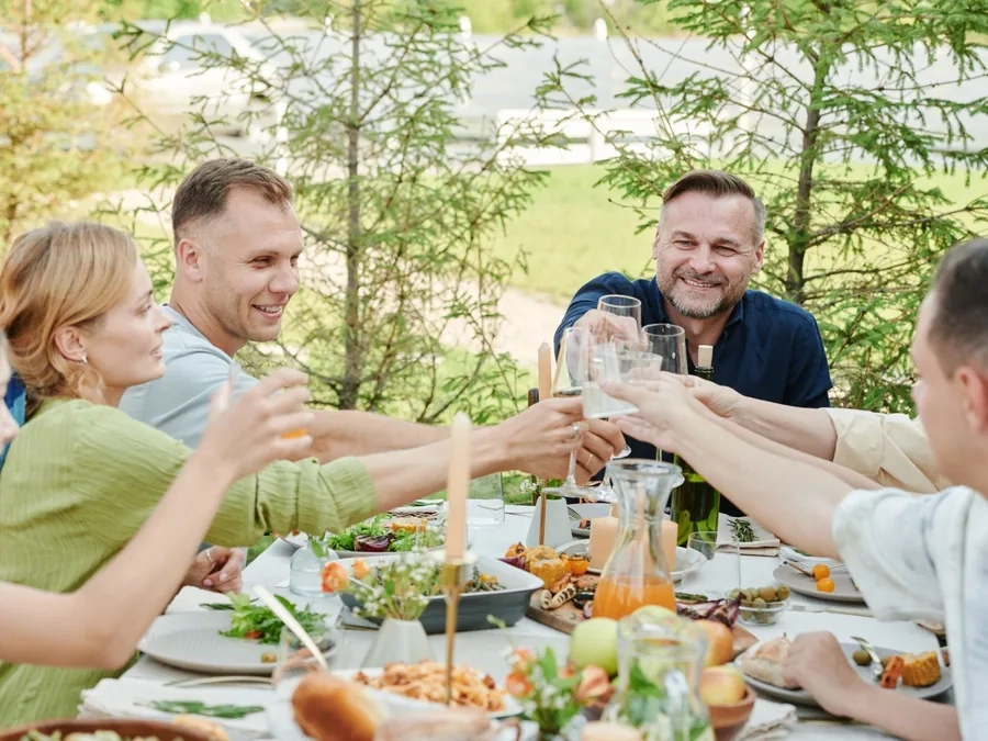 Friends around an outdoor lunch table clinking glasses in a toast