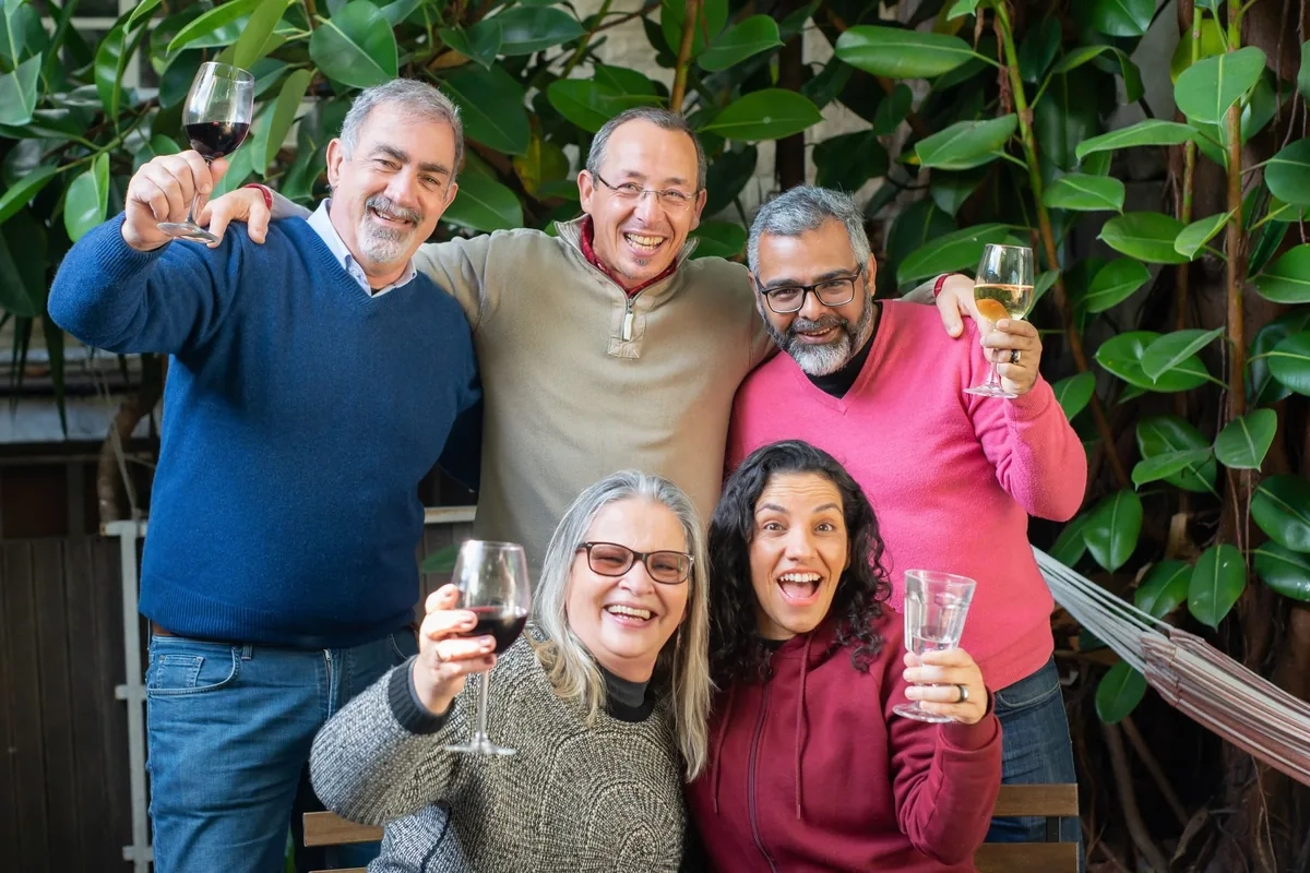 Friends of different ages laughing and raising glasses together in a leafy garden
