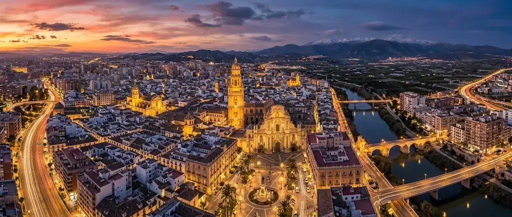 Vista aérea de Murcia al atardecer, con la catedral iluminada y el río Segura cruzando la ciudad