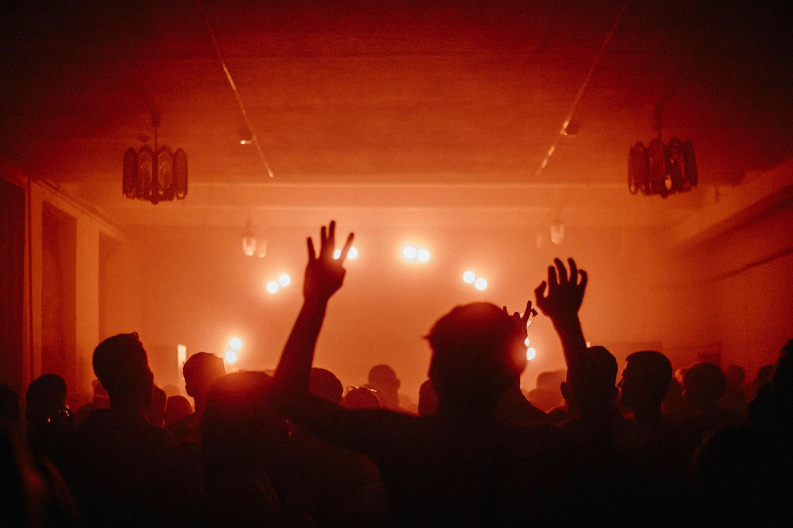 Silhouettes of people dancing with their hands in the air under warm red lights