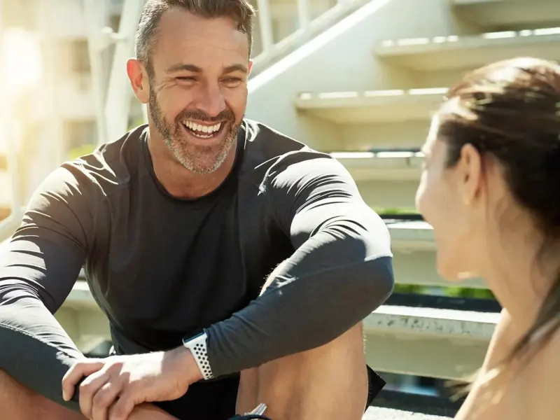 A smiling man in his 40s chatting with a woman on outdoor stairs after a workout