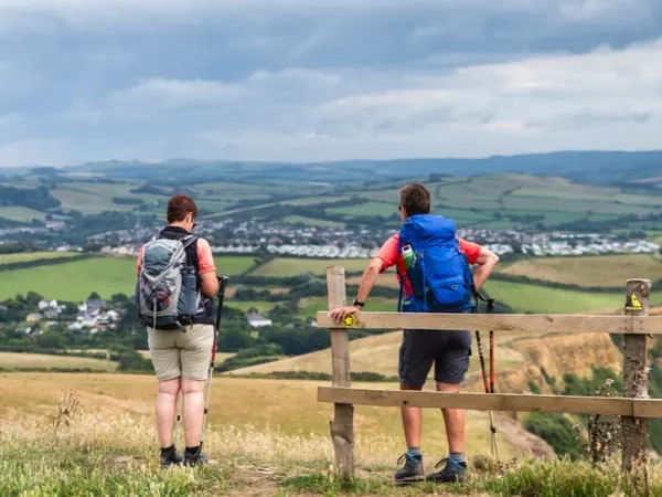 Two walkers stopped at a stile on a hill path, looking out across a wide valley