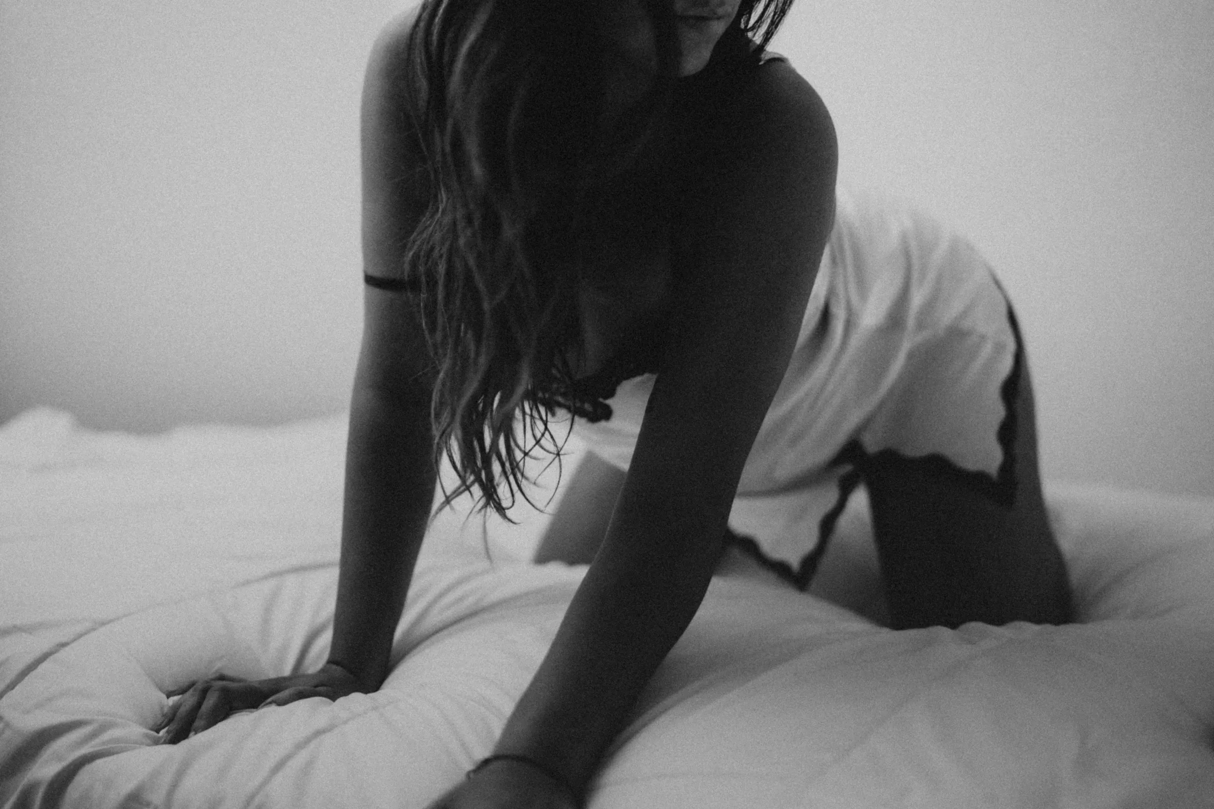 Una mujer en ropa interior sobre una cama deshecha, fotografiada en blanco y negro.