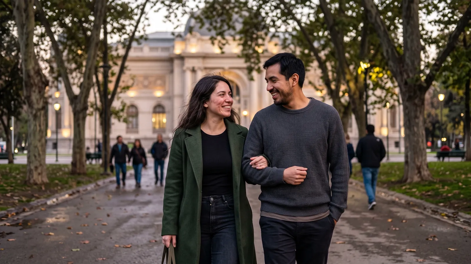 Una pareja camina del brazo bajo los plátanos del Parque Forestal de Santiago al anochecer, con un edificio histórico iluminado al fondo (imagen generada por IA)