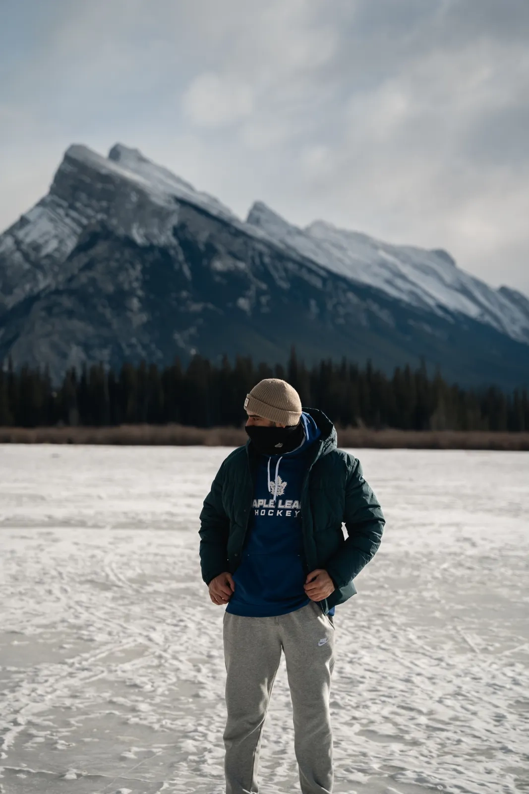 Person in a dark jacket on a snowy lakeshore with rugged mountains behind