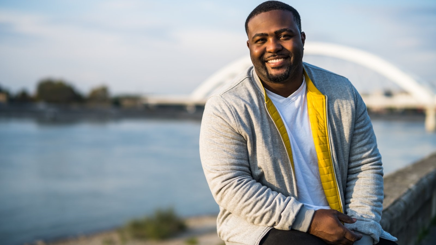 A man smiling outdoors by the water